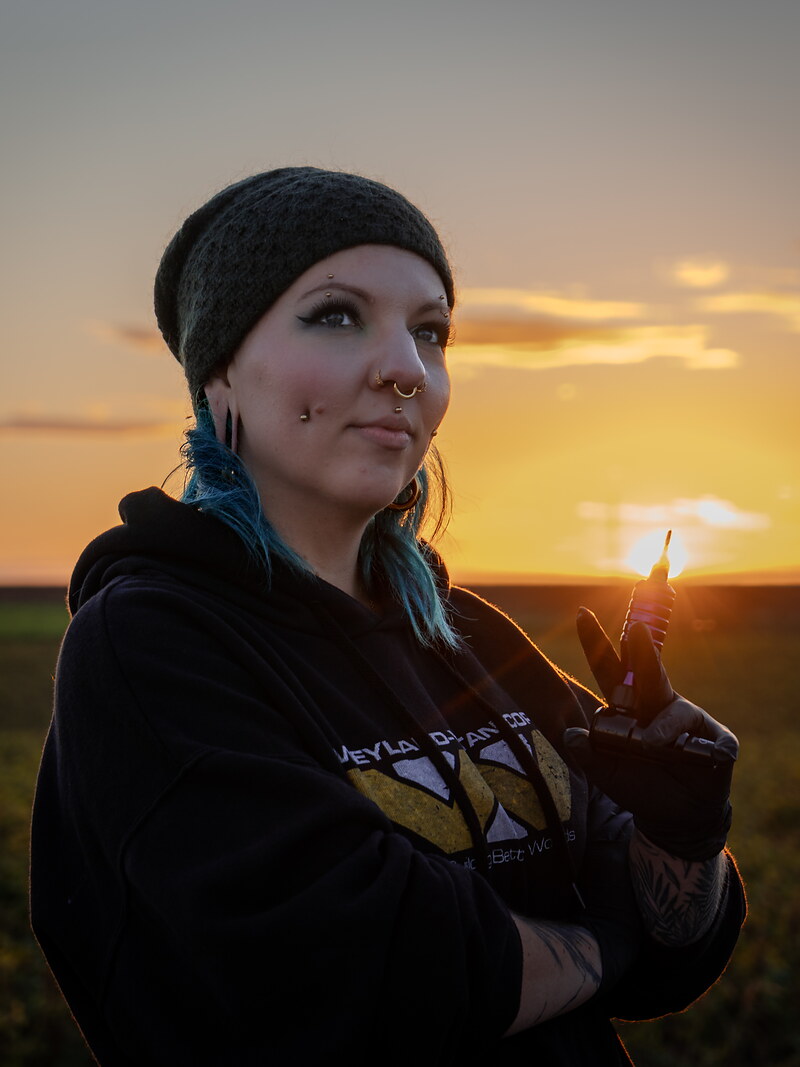 Sophie Guiot, tatoueuse à Andenne, dermographe en main devant un coucher de soleil